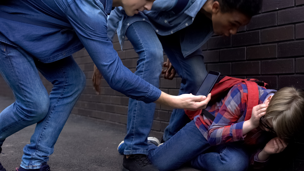 Two teenagers harassing and filming another teenager on the ground, depicting the serious issue of felony making criminal threats.