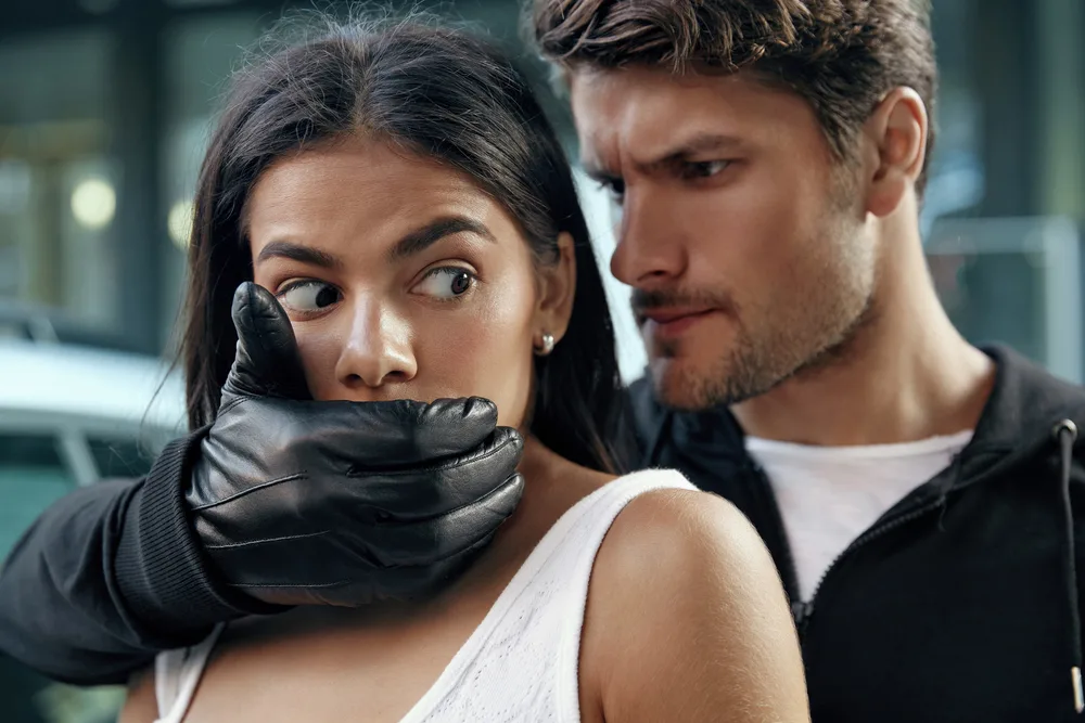 A man forcefully covering a woman's mouth with his hand, representing the concept of felony making criminal threats.
